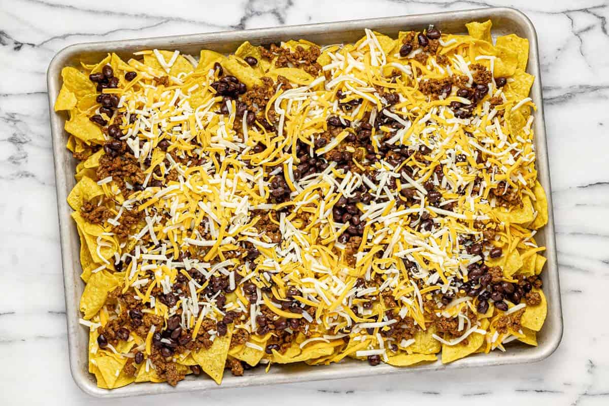 Sheet pan with chips, shredded cheese, taco meat, and black beans. 