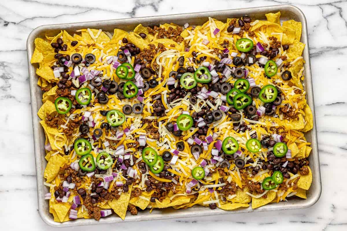 Sheet pan with layers of ingredients to make loaded nachos. 