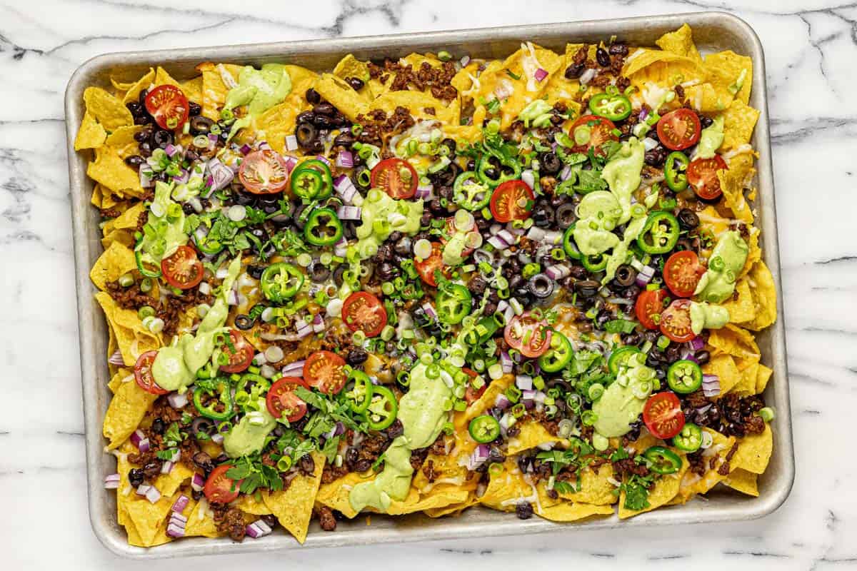 Freshly baked loaded nachos with tomatos, herbs, and avocado sauce. 