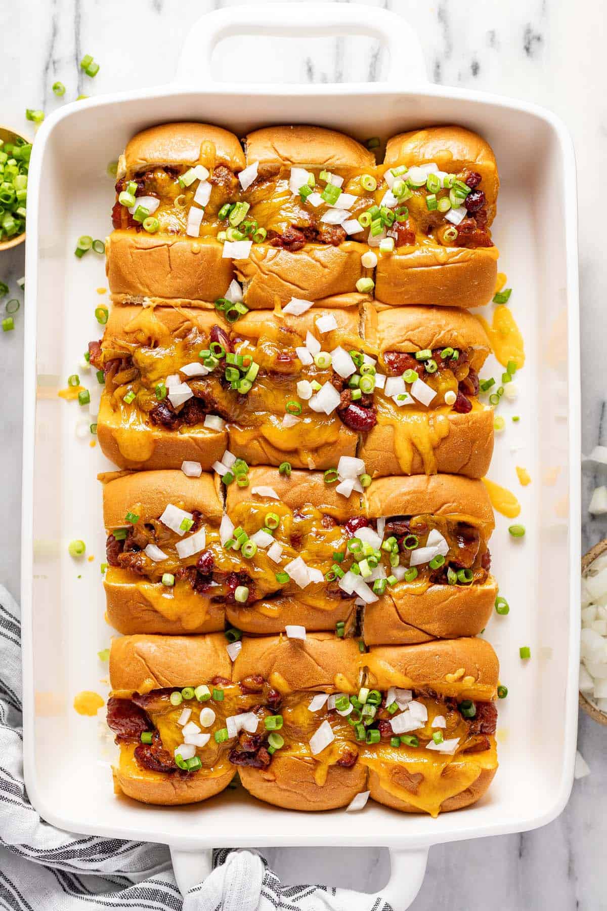 Baking dish filled with mini chili cheese dogs topped with diced onion and green onion. 