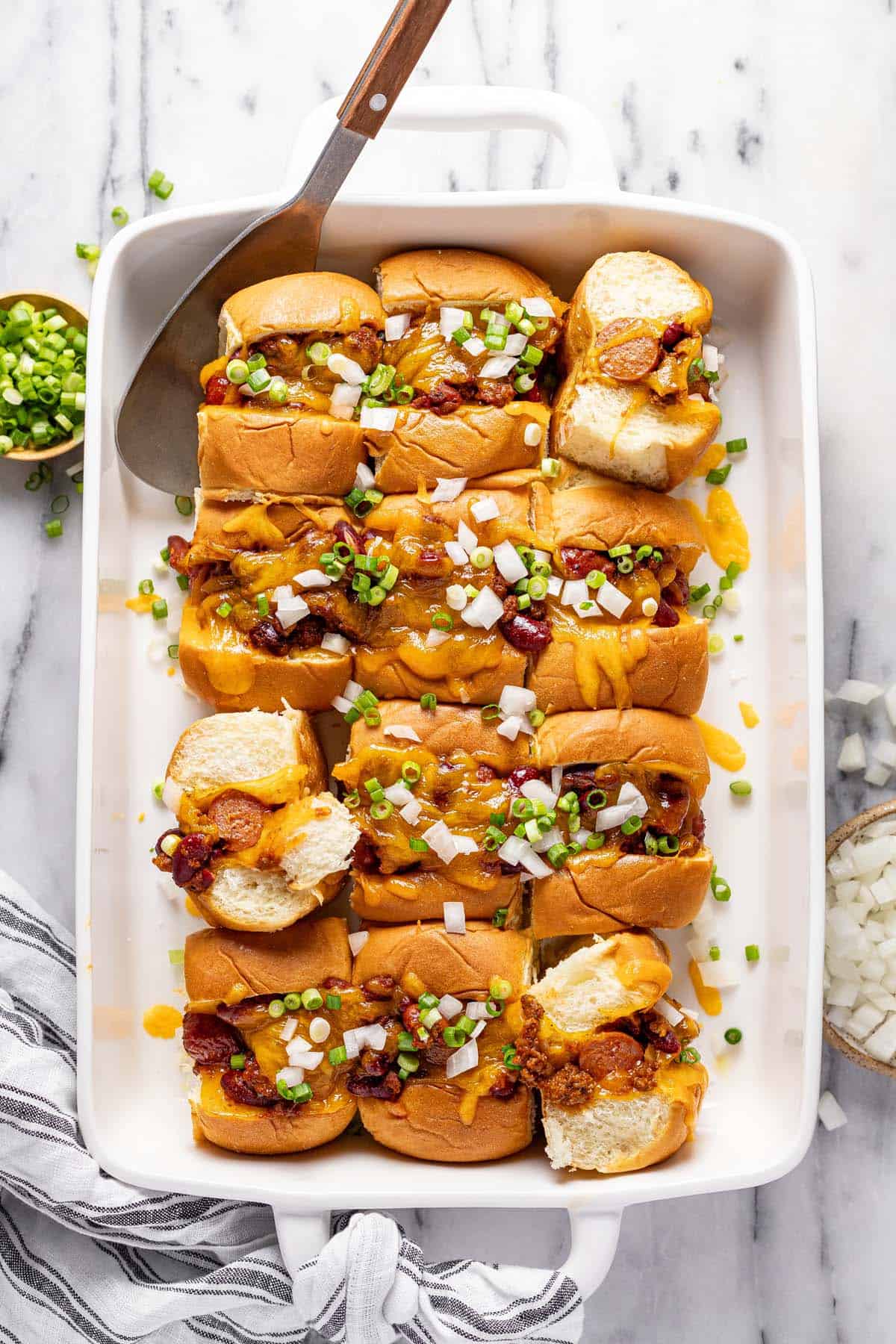 Baking dish filled with mini chili cheese dogs topped with diced onion and green onion. 