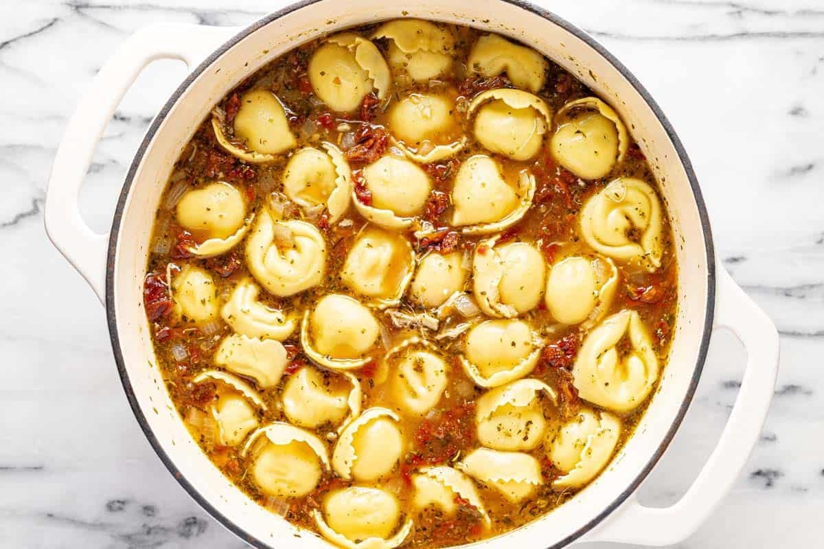 Cooked tortellini in a sun-dried tomato broth in a large pot. 