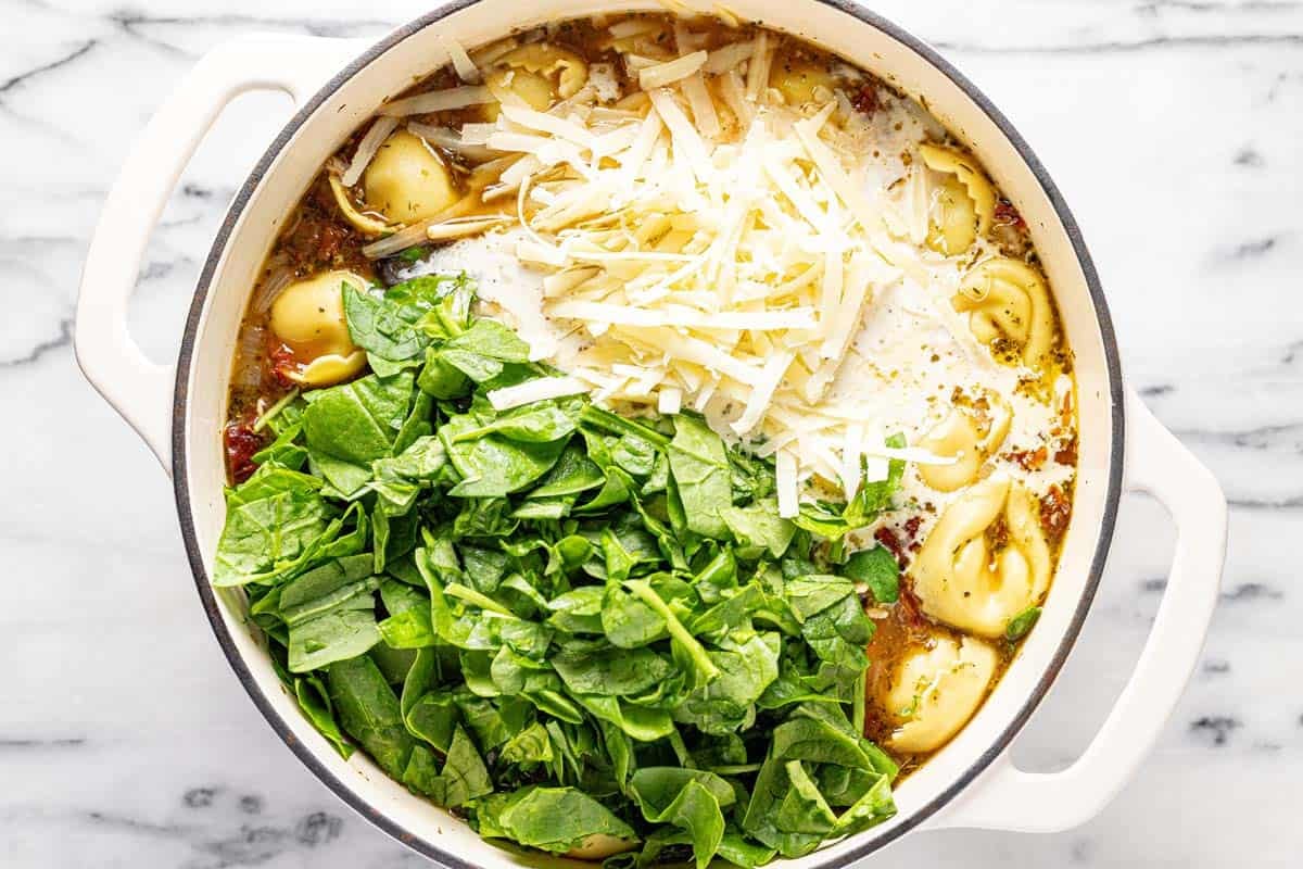 Heavy cream, spinach, and Parmesan added to a large pot of tortellini soup. 