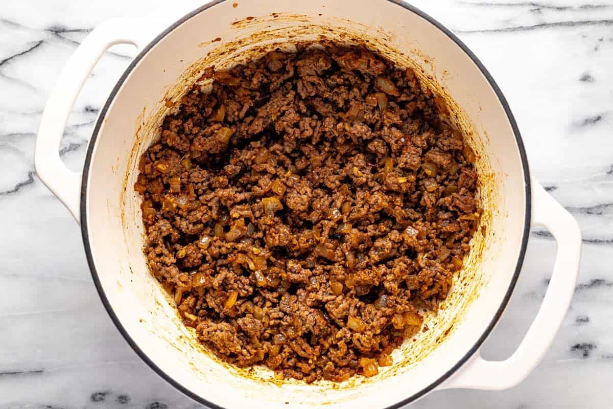 Browned ground beef in a large pot with veggies and tomato paste. 