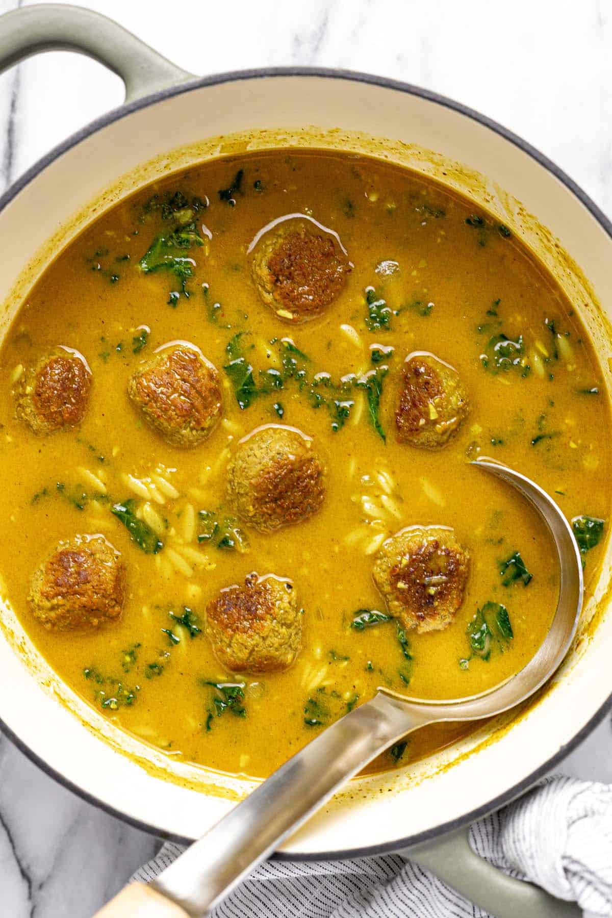 Large pot of creamy curry meatball soup with orzo and kale. 