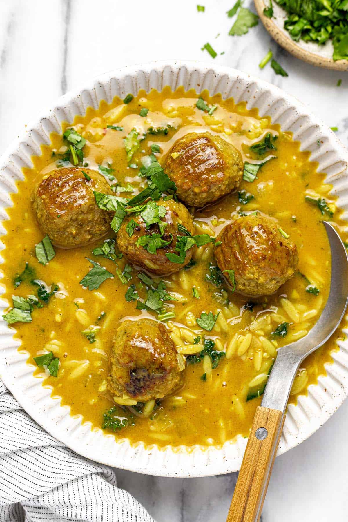 Bowl of curry meatball soup garnished with chopped cilantro. 