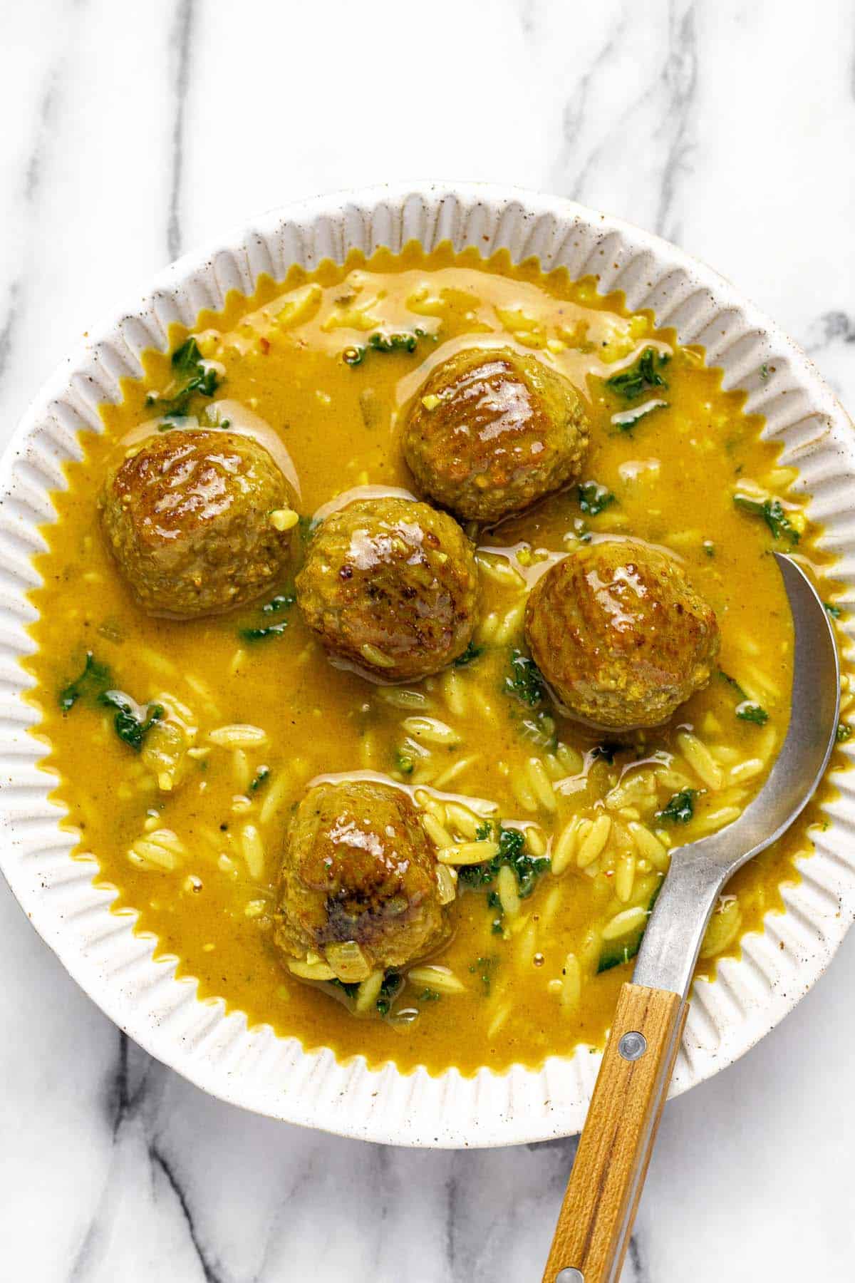 A bowl of curry meatball soup with a spoon.