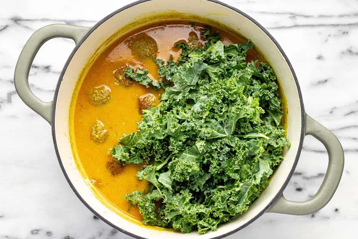 Fresh kale being added to a large pot of meatball soup. 