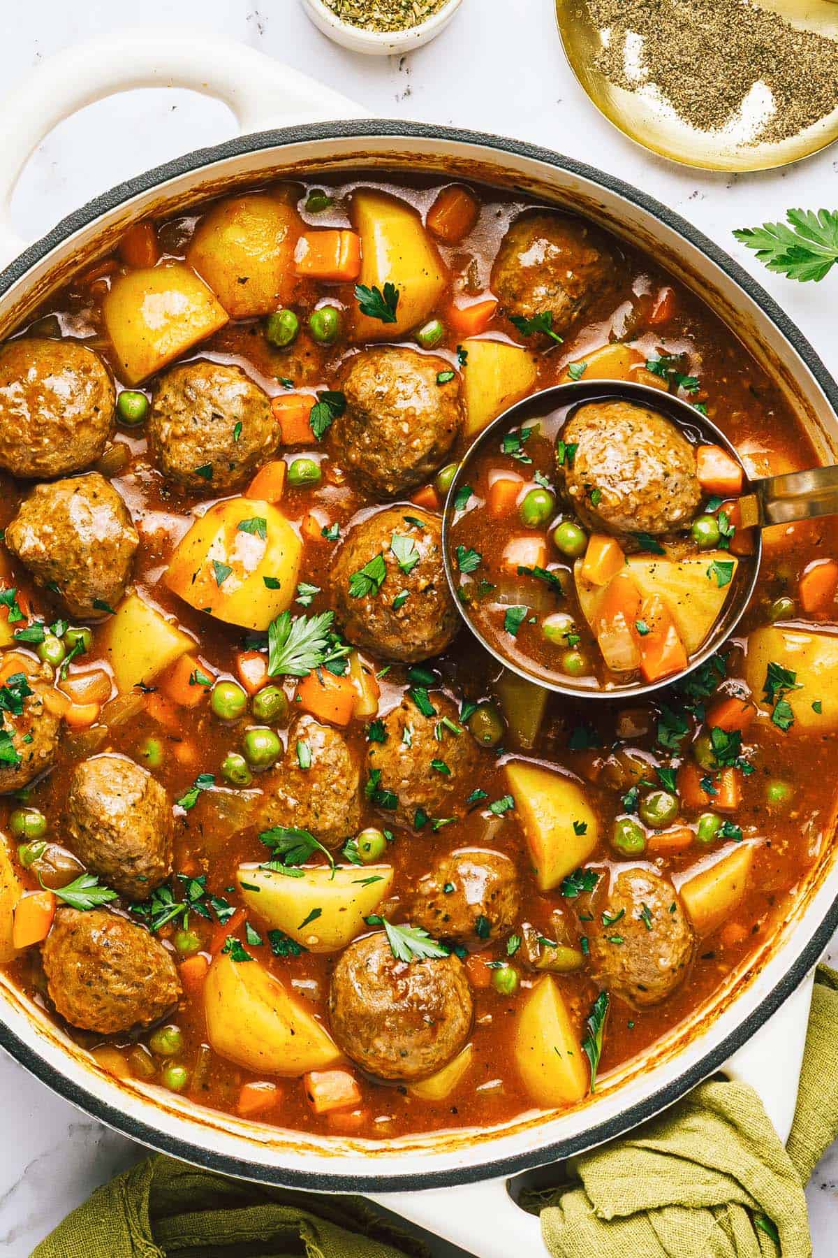 Close up shot of a pot of meatball stew with a ladle in it. 