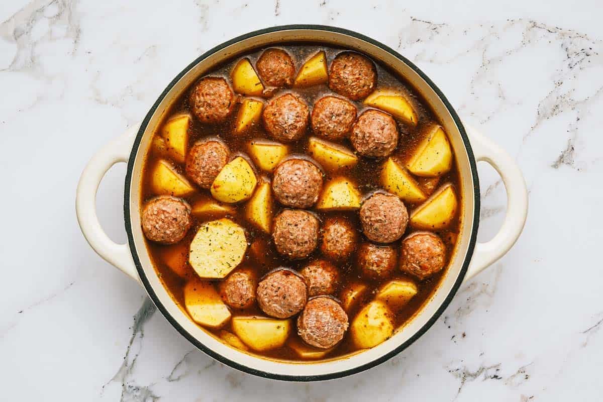 Meatballs, potatoes, and broth in a large pot. 