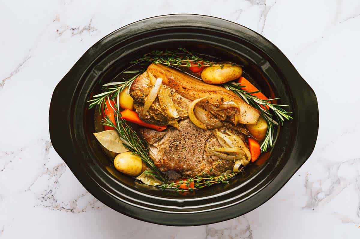 Slow cooker with meat, veggies, and herbs. 