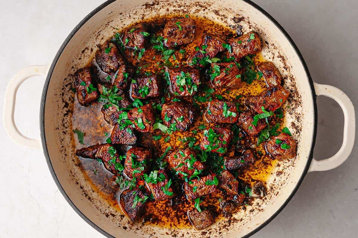 Steak bites garnished with fresh parsley in a large pan. 