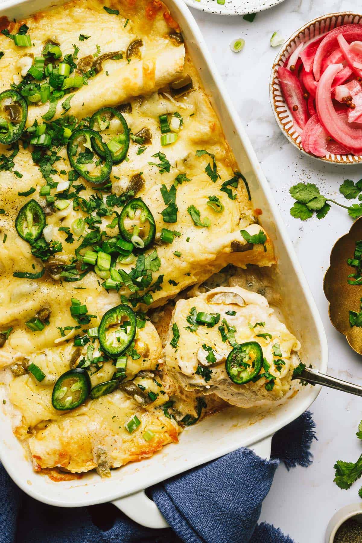 A spoon taking chicken enchiladas out of a large baking dish. 