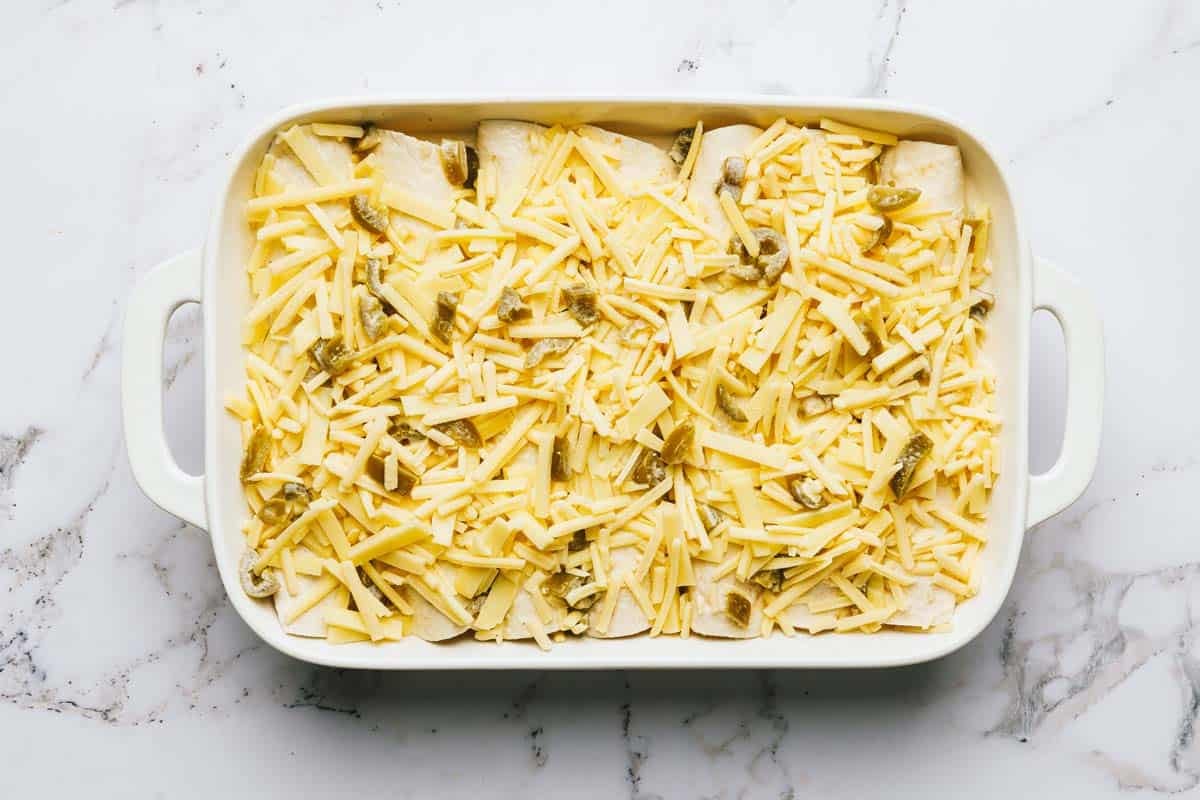 Chicken enchiladas topped with white sauce and shredded cheese. 