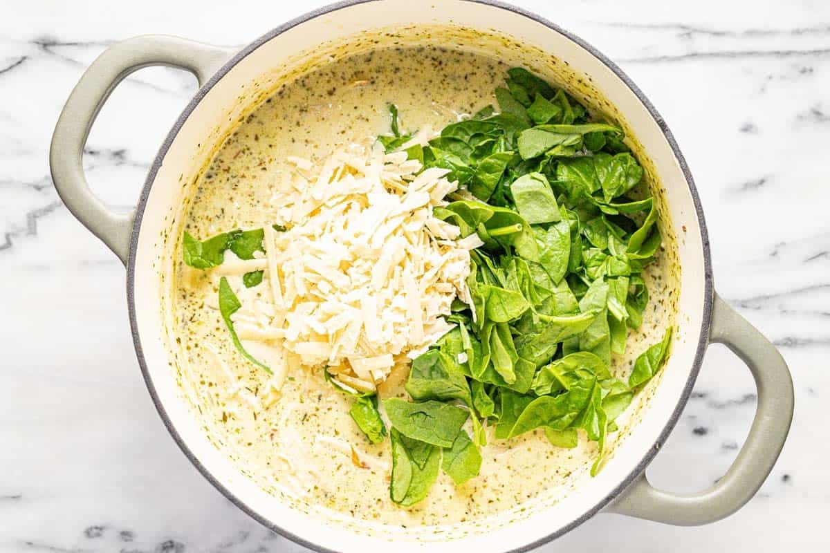 Parmesan cheese and chopped spinach added to a large pot of soup. 