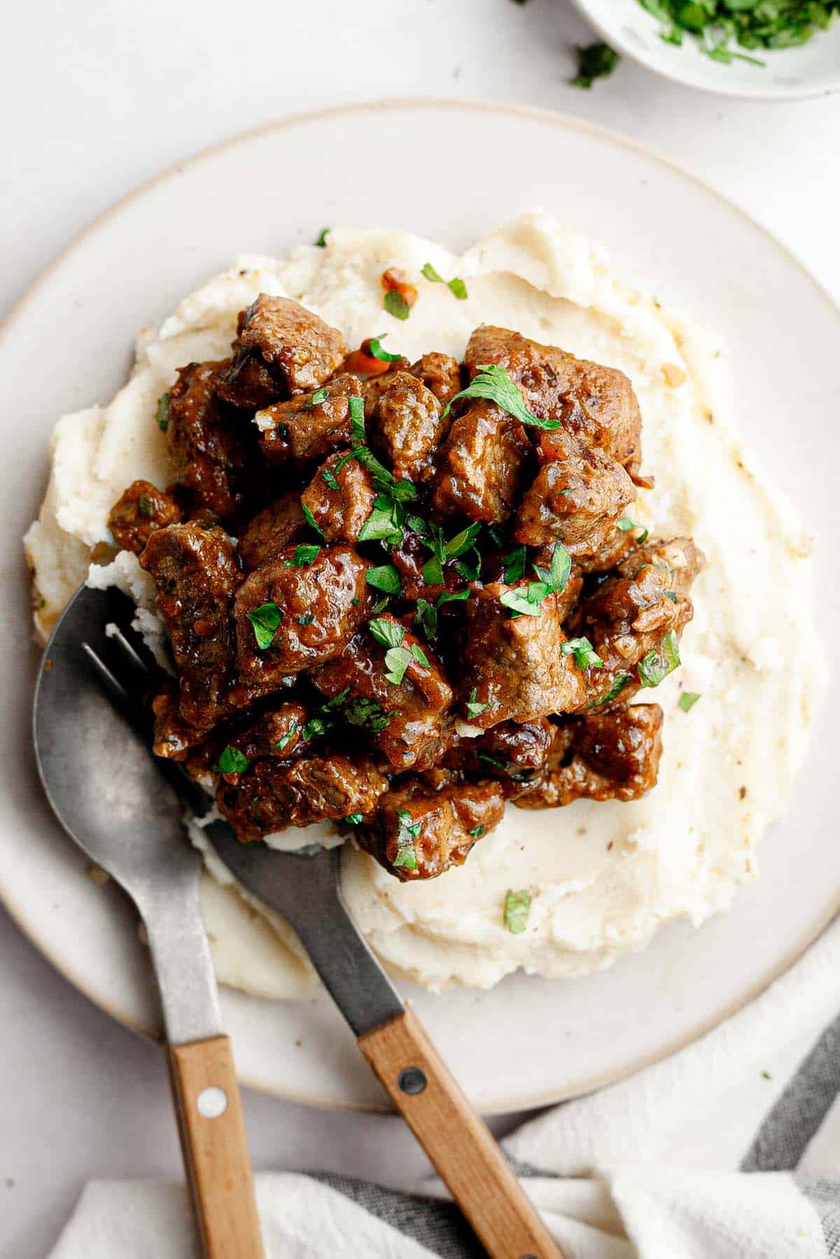 Plate with mashed potatoes and beef tips garnished with parsley. 