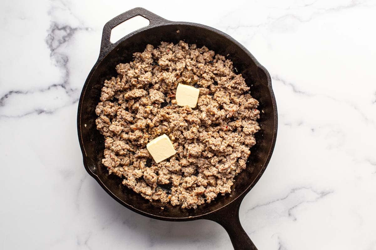 Cooked ground sausage with butter and spices in a cast iron skillet. 