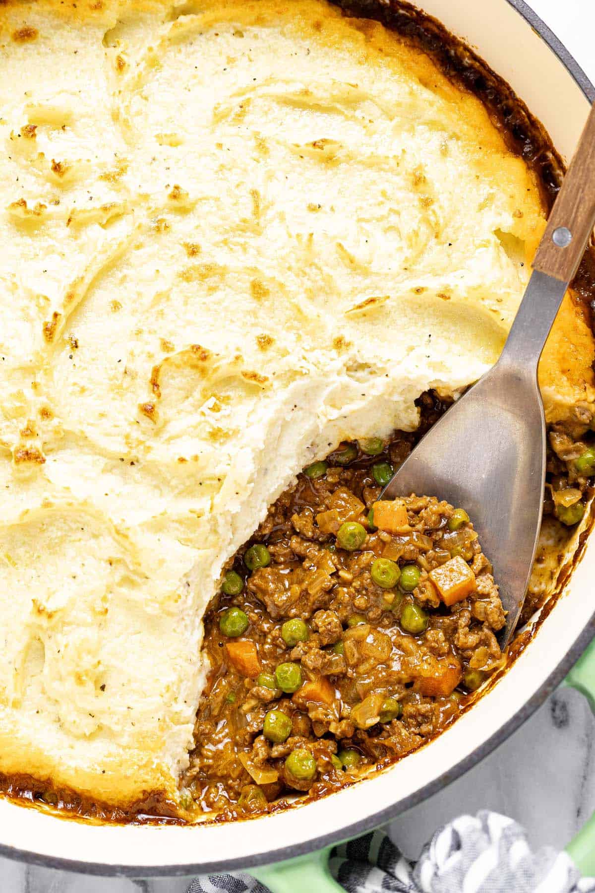 Close up shot of a pan of cottage pie with a spoon in it. 