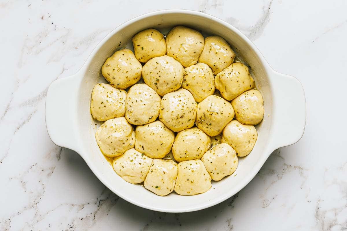 Pizza bites in a large pan topped with garlic butter and seasoning. 