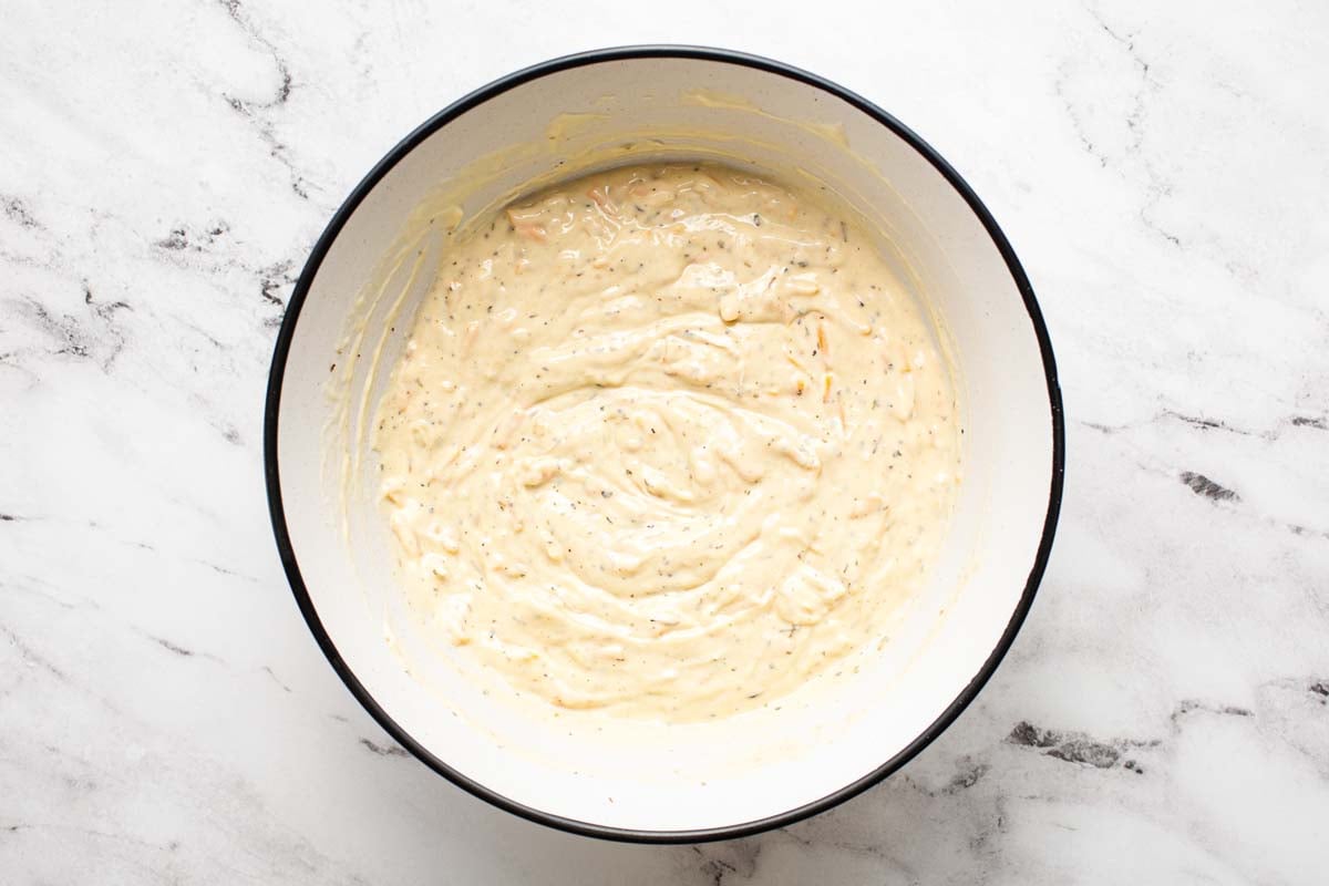 Condensed soup, half and half, cheese, and spices mixed in a bowl. 