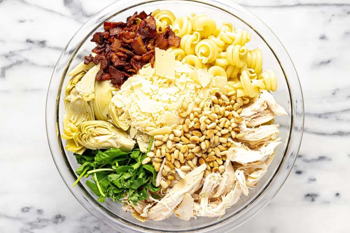 Ingredients to make chicken bacon artichoke pasta salad in a large bowl. 