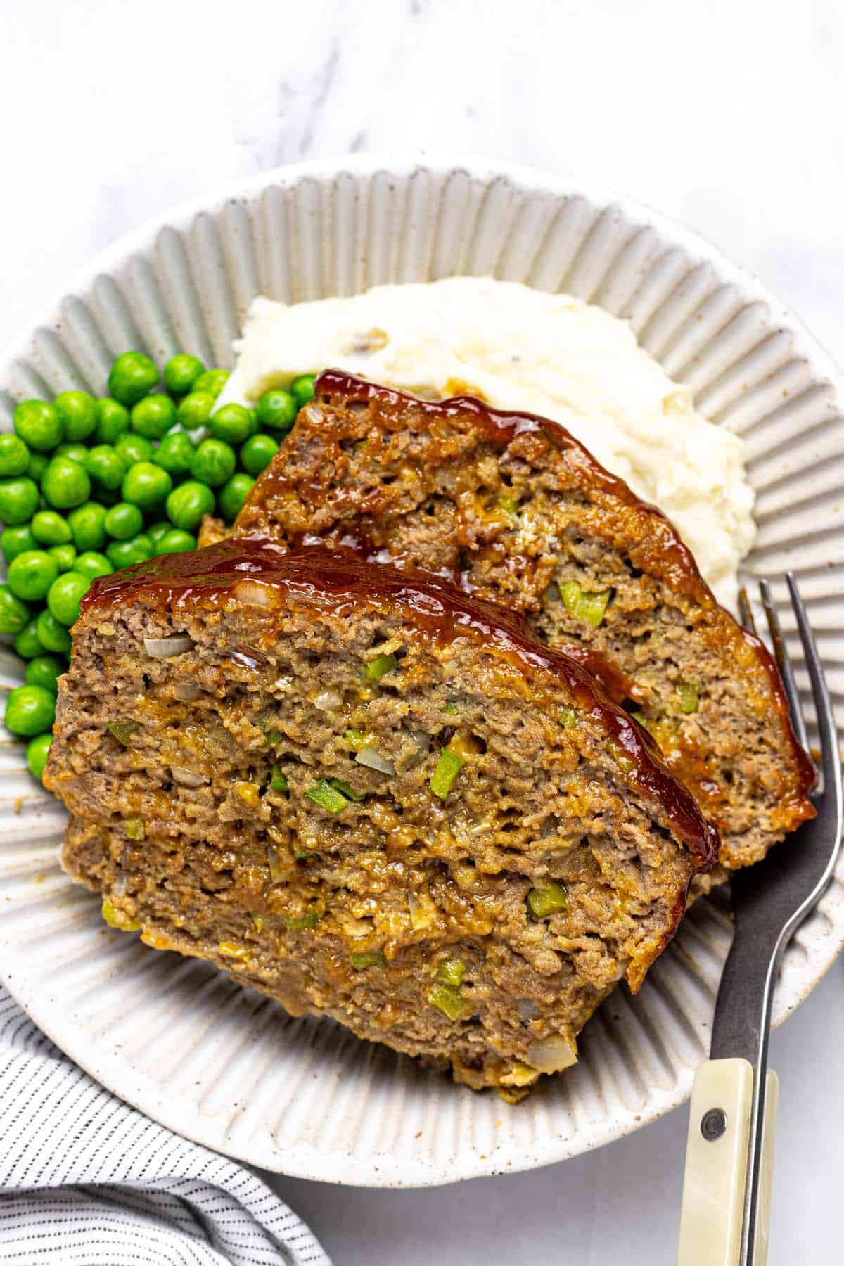 Plate with 2 slices of meatloaf, peas, and mashed potatoes. 