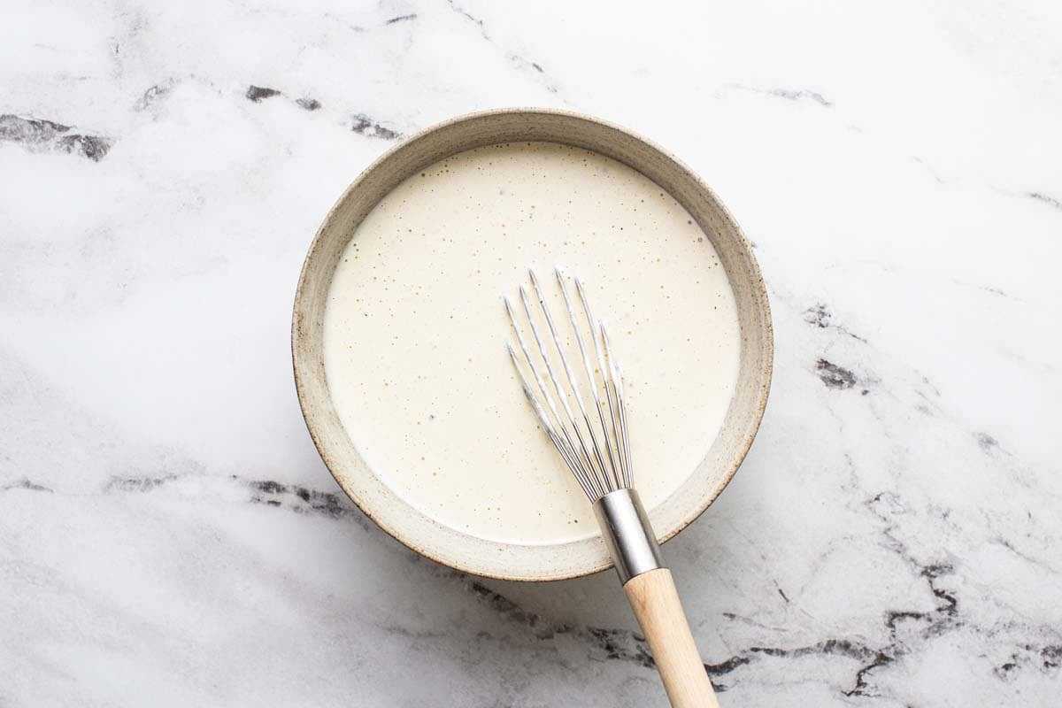 Creamy pasta salad dressing in a bowl with a whisk. 