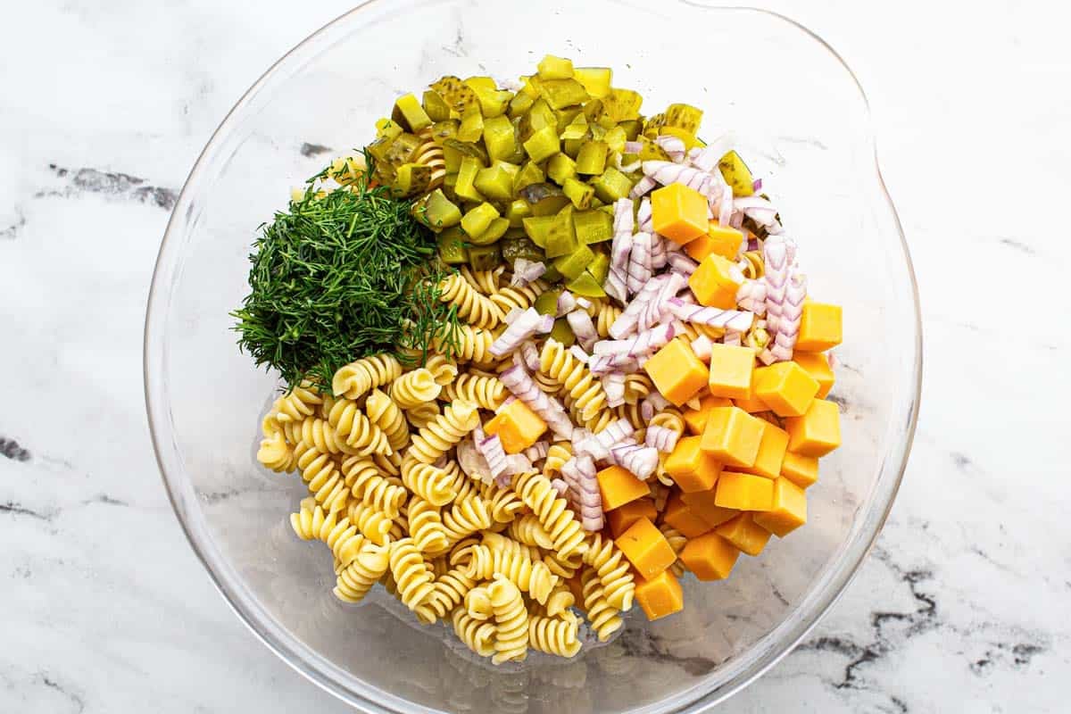 Large bowl with ingredients to make dill pickle pasta salad. 