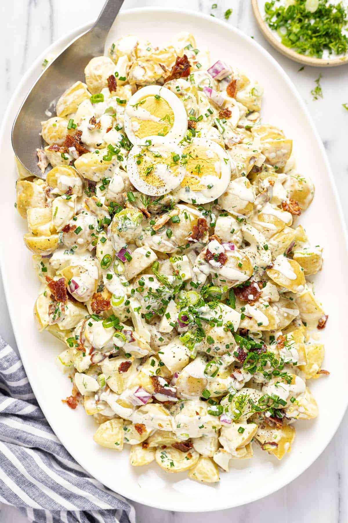 Serving platter with homemade potato salad topped with sliced eggs. 