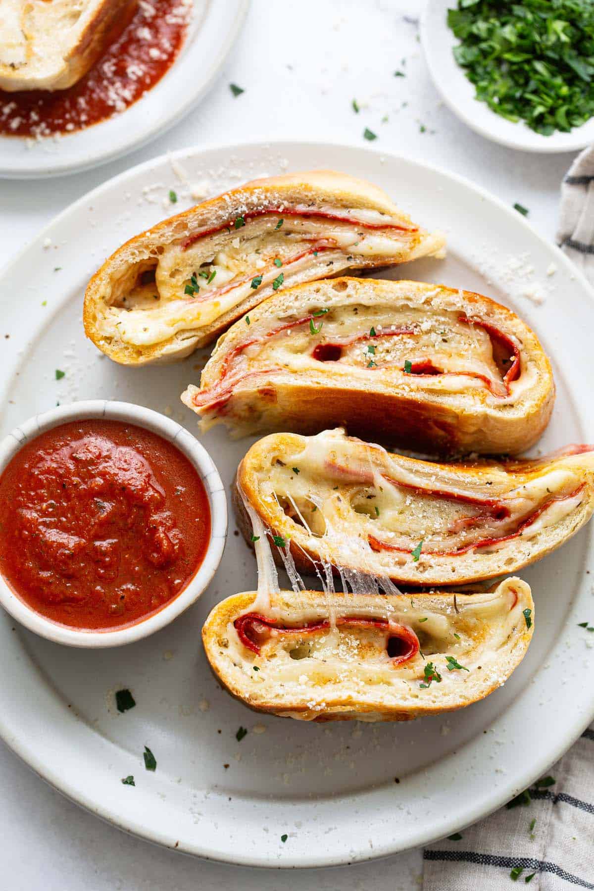 A plate with stromboli slices and a bowl of pizza sauce. 