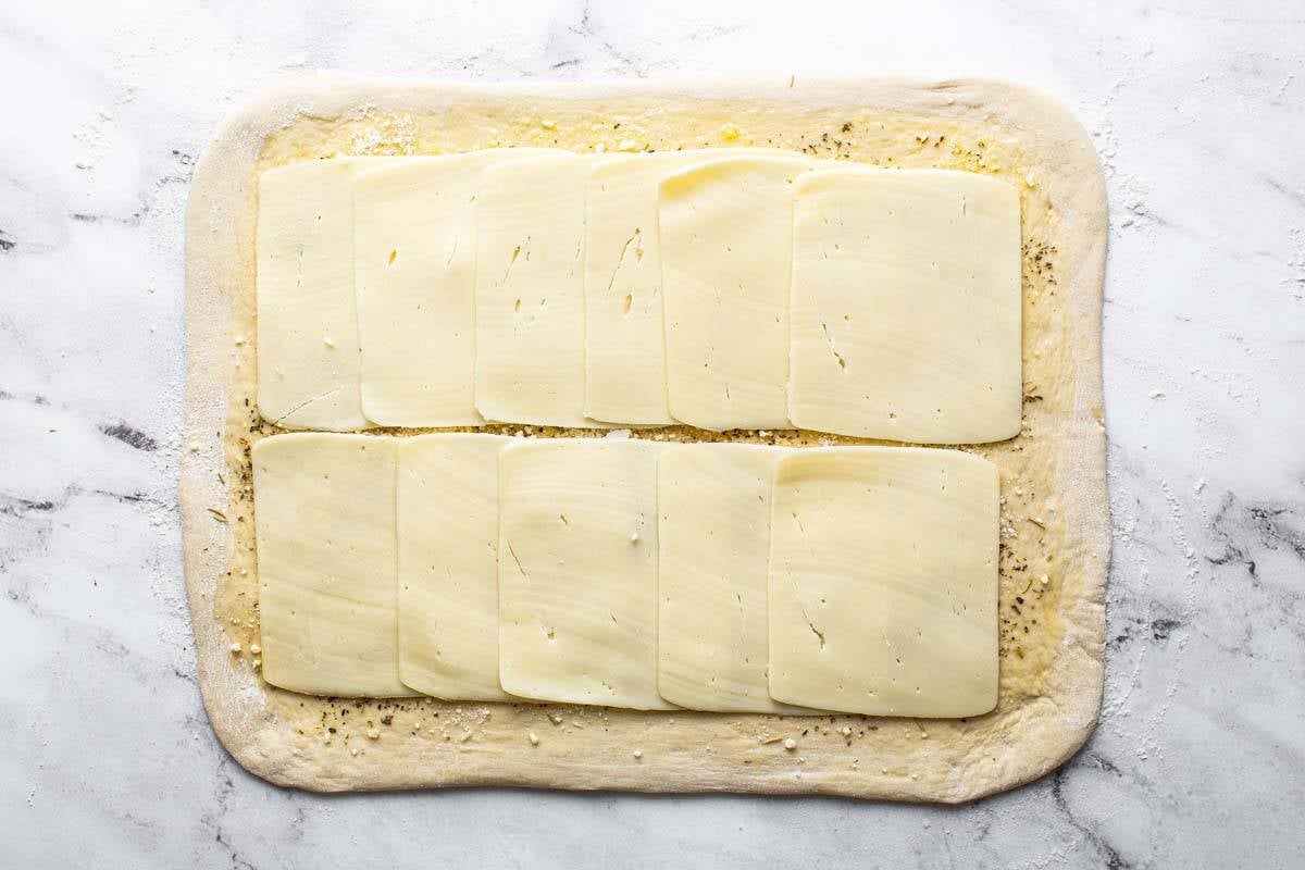 Slices of cheese on top of pizza dough. 