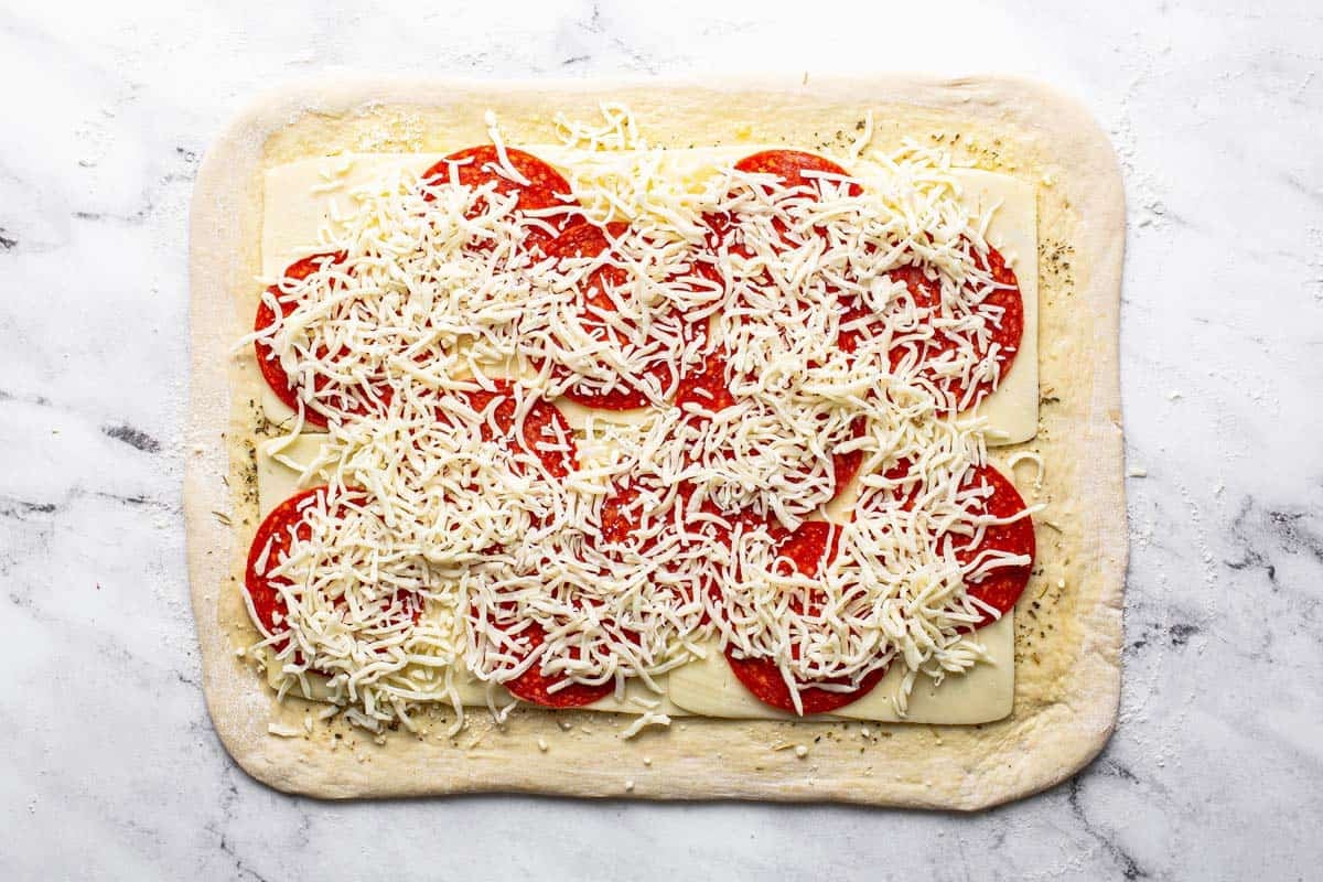 Rolled out pizza dough with cheese and pepperoni on it. 