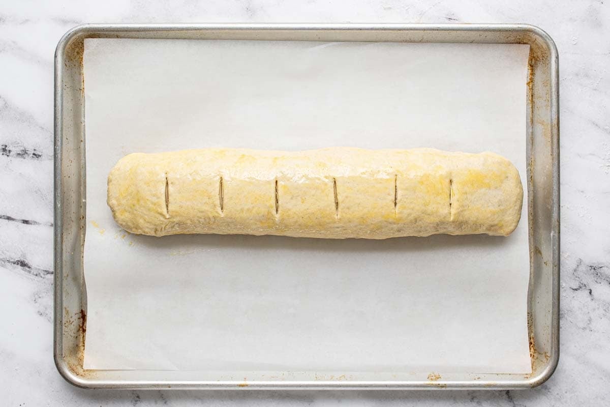 A rolled up stromboli on a parchment lined baking sheet. 