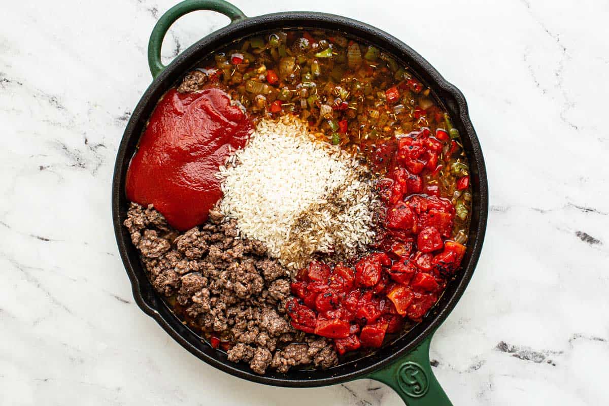 Beef, rice, tomato sauce, and tomatoes in a large pan with veggies. 