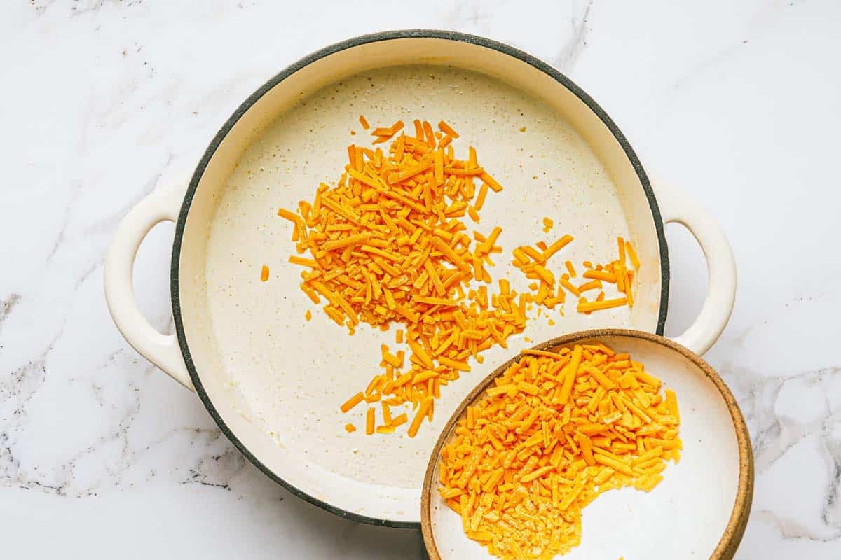 Shredded cheese being added to a pan of cream sauce.