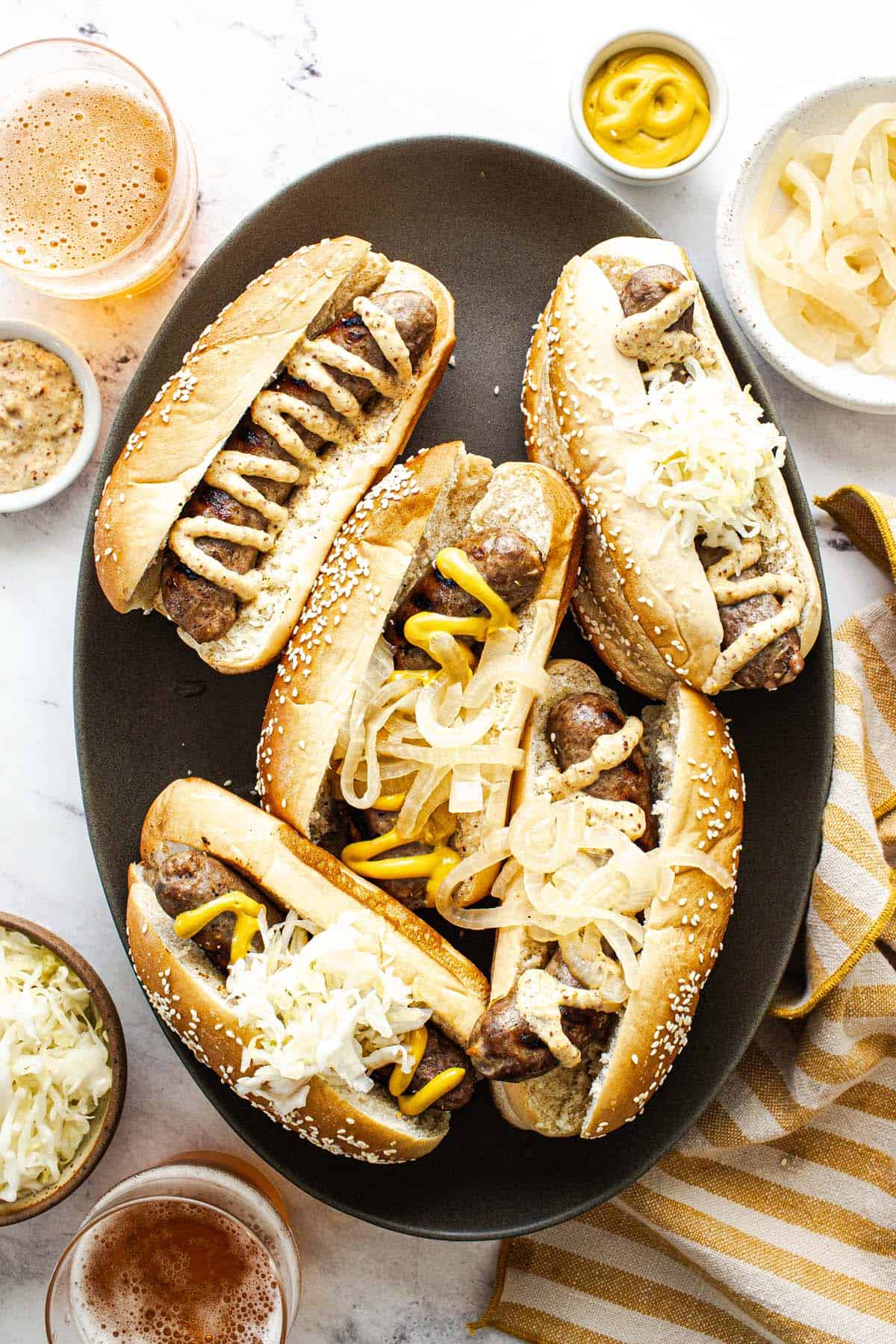 Large platter filled with beer brats topped with mustard, sauerkraut, and onions.