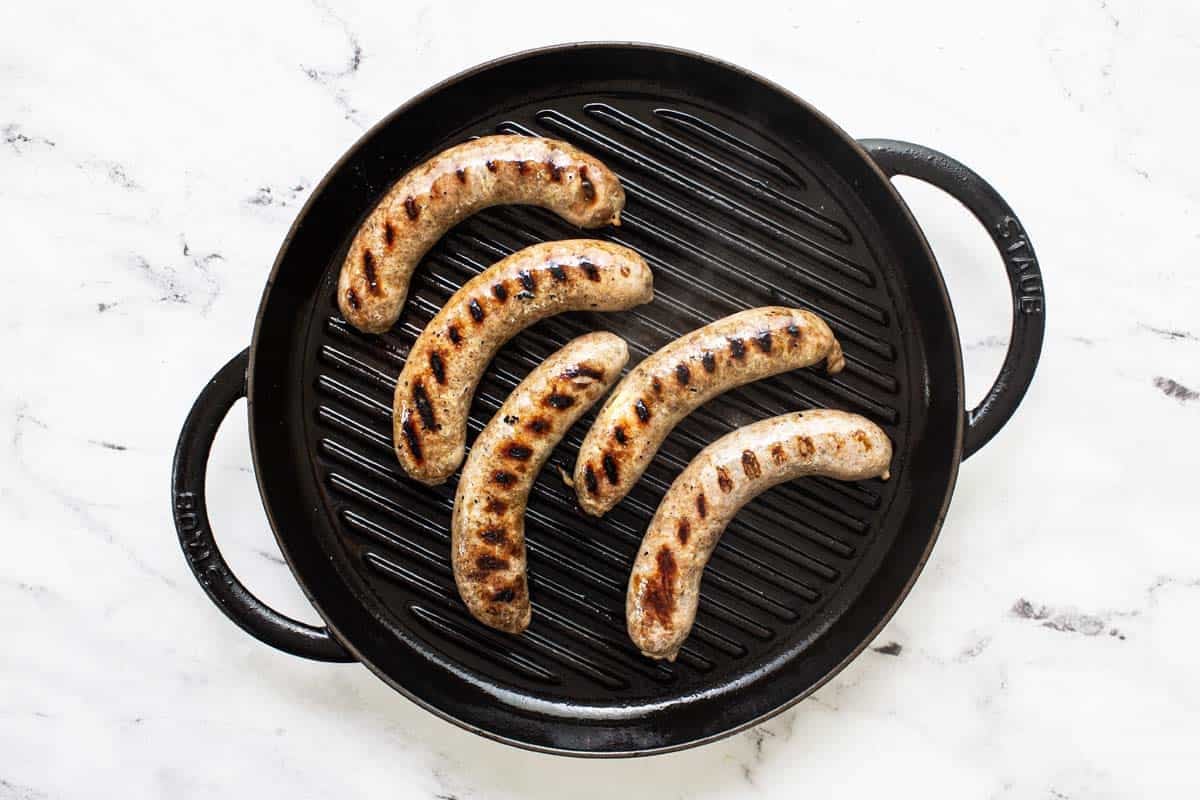 Large saute pan with grilled beer-broiled brats. 