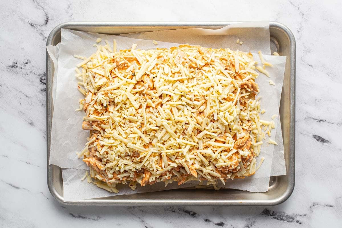 Shredded cheese on top of buffalo chicken sliders. 