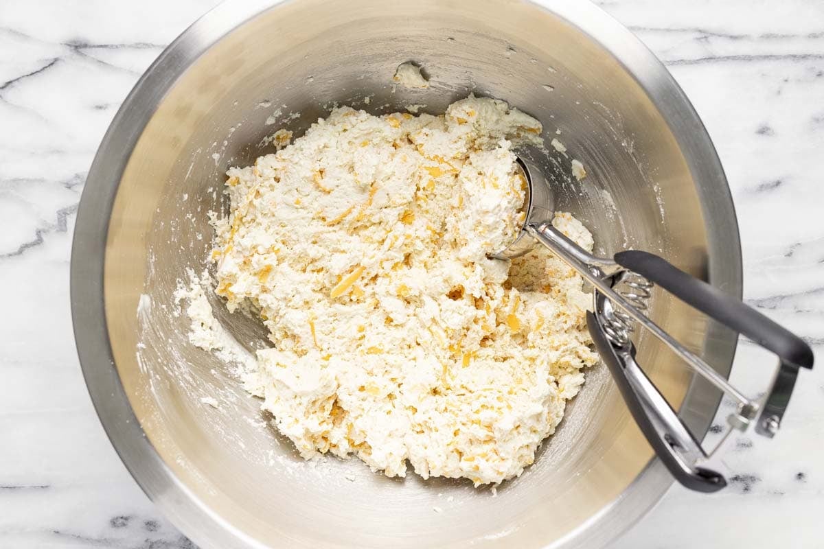 Large bowl with biscuit dough and a cookie scoop in it. 