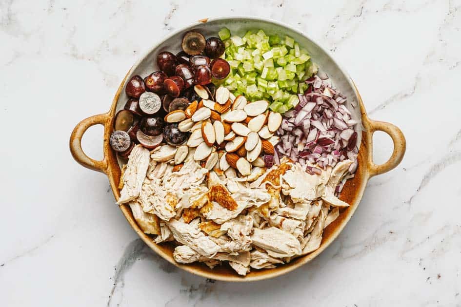 Bowl filled with rotisserie chicken, almonds, onion, grapes, and celery. 