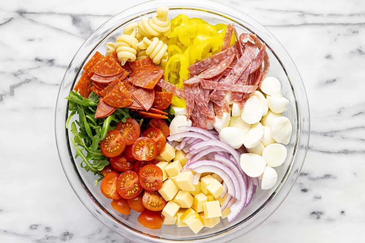 Large bowl filled with ingredients for grinder pasta salad. 