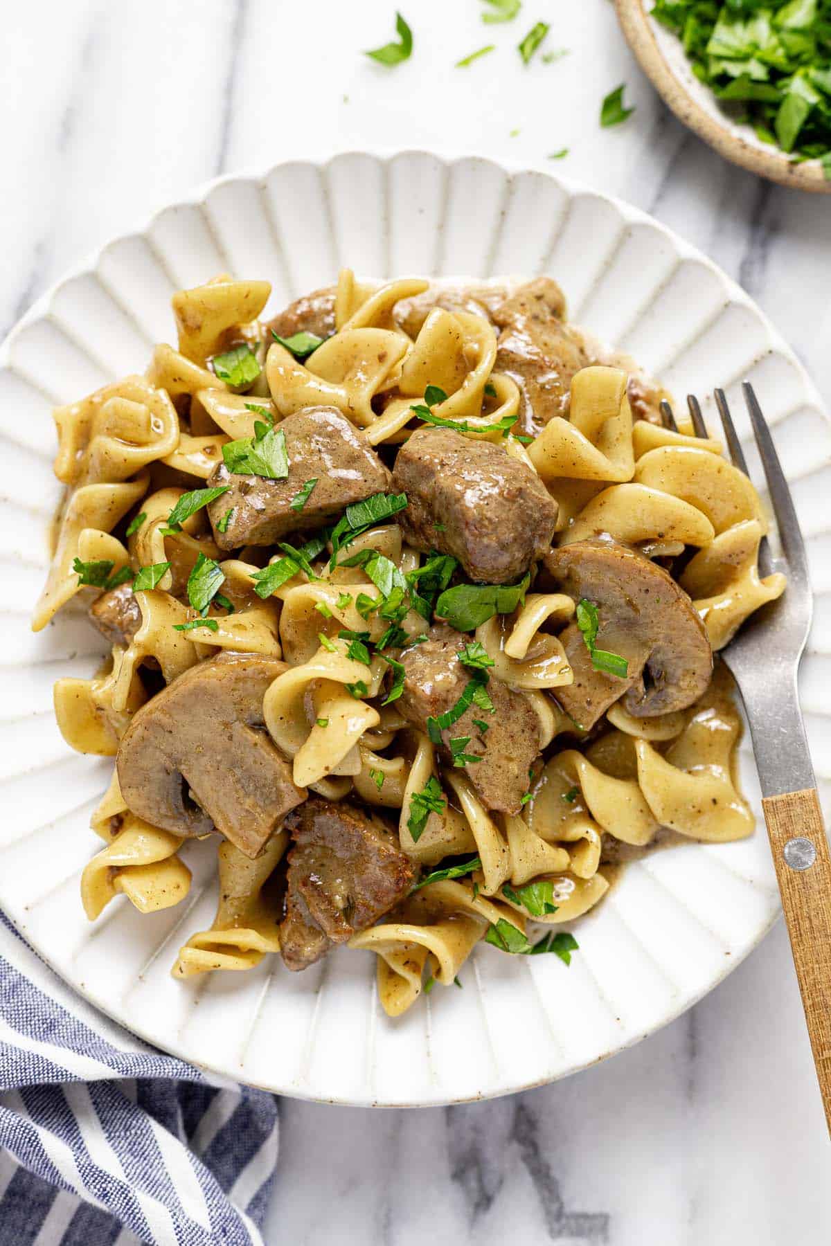 Plate with slow cooker beef and noodles garnished with fresh parsley. 