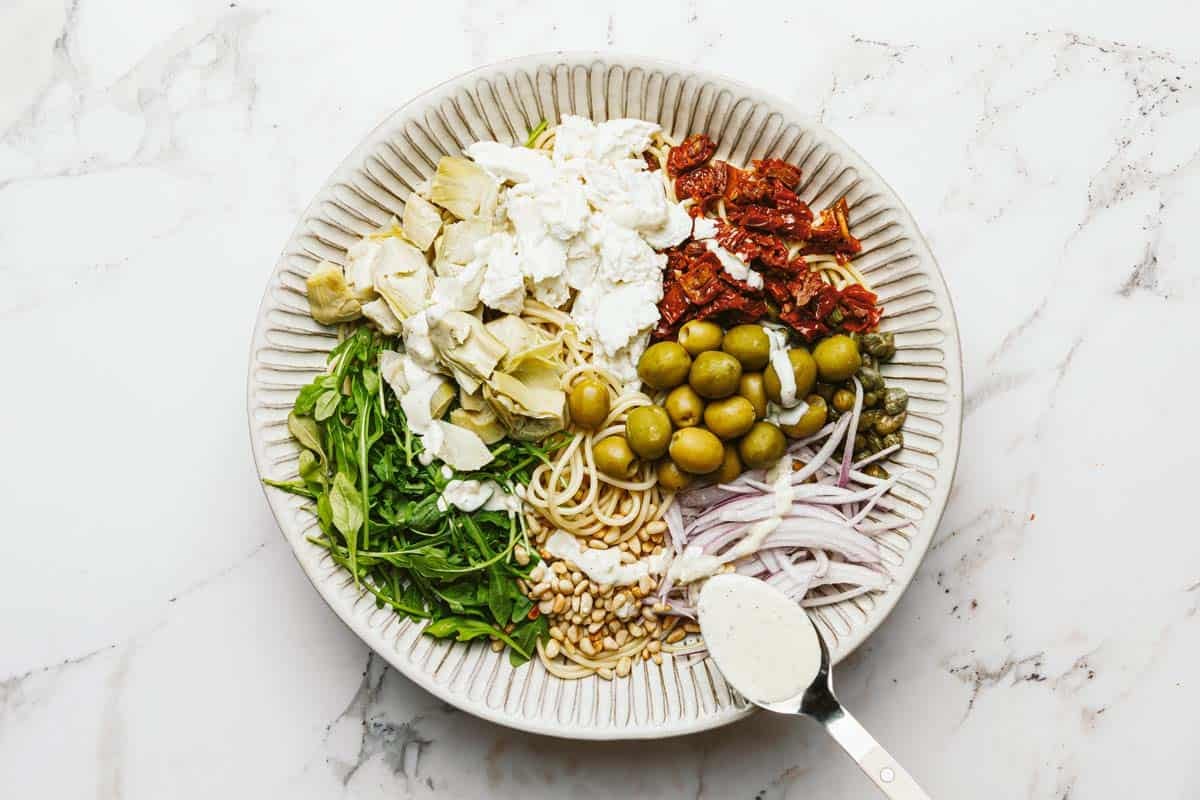 Bowl of pasta salad ingredients with creamy dressing being drizzled over it.