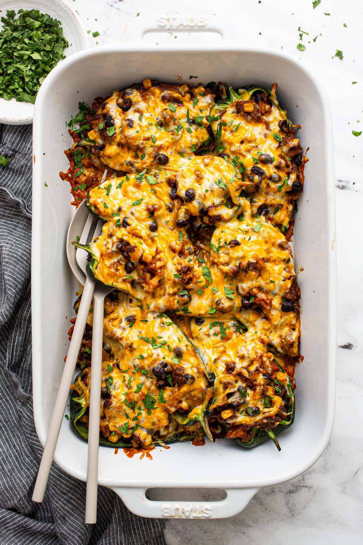 Baking dish filled with stuffed poblano peppers garnished with cilantro. 