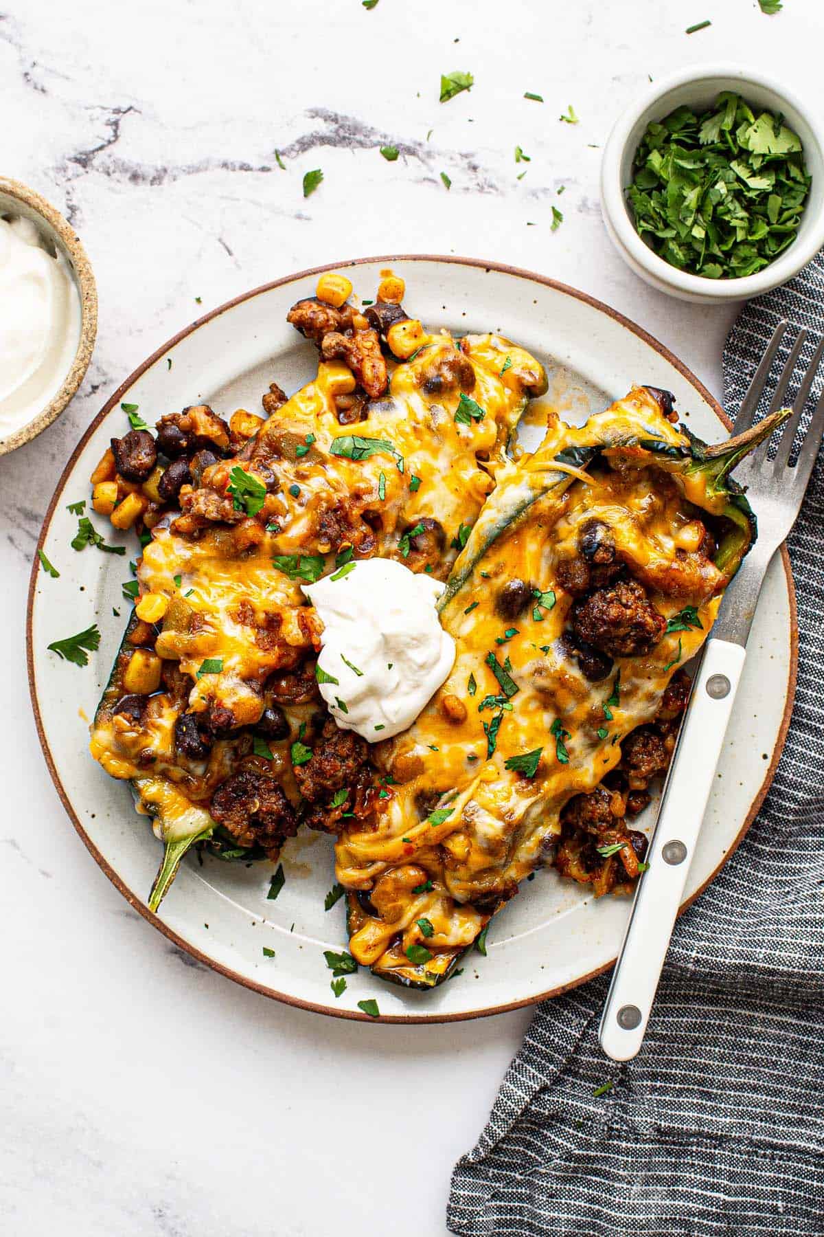 Plate with 2 stuffed peppers garnished with sour cream and fresh cilantro. 