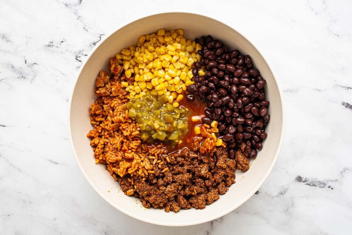 Seasoned ground beef, rice, corn, black beans, and green chiles in a large bowl. 