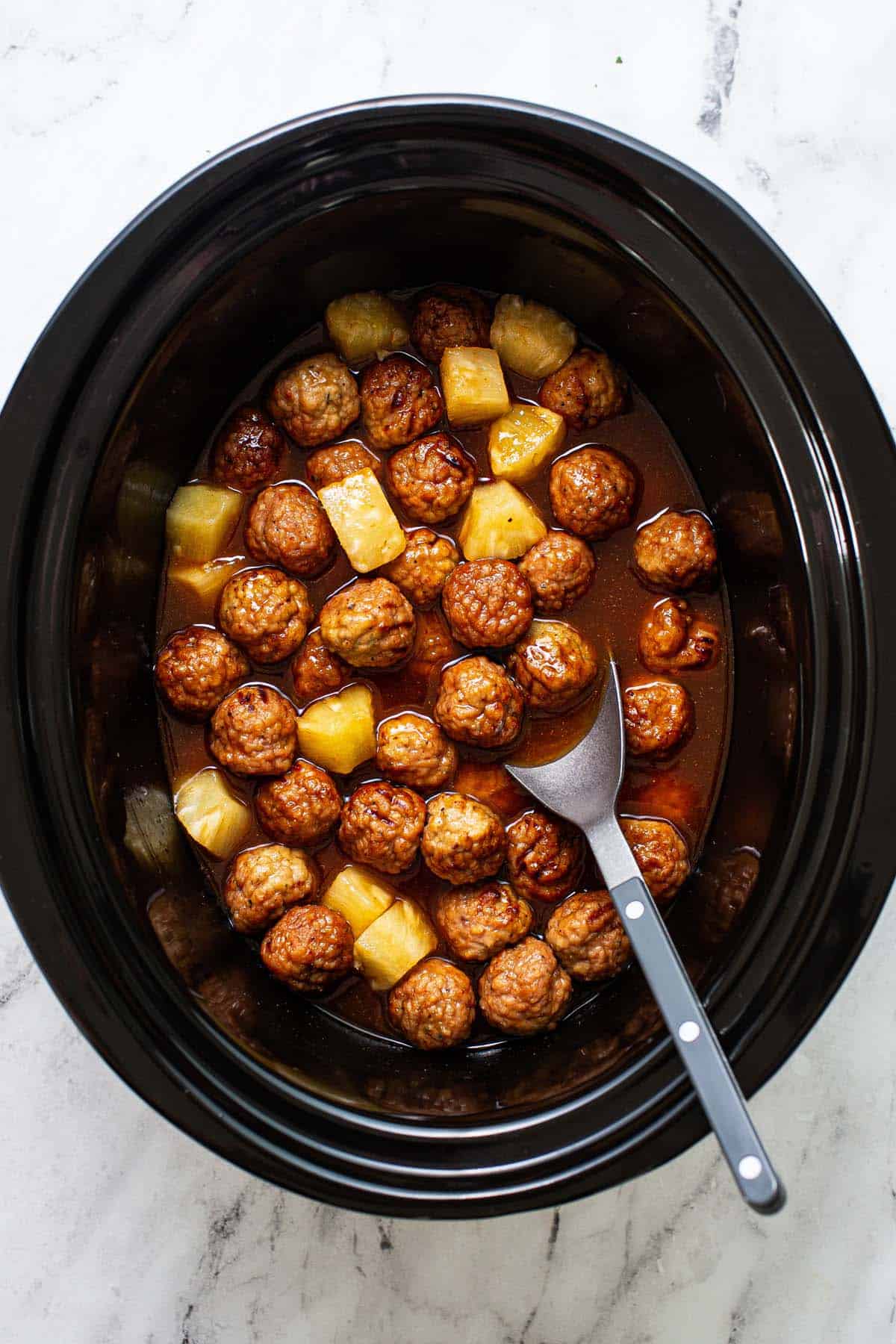 Large corck pot filled with sweet and sour meatballs with pineapple chunks. 