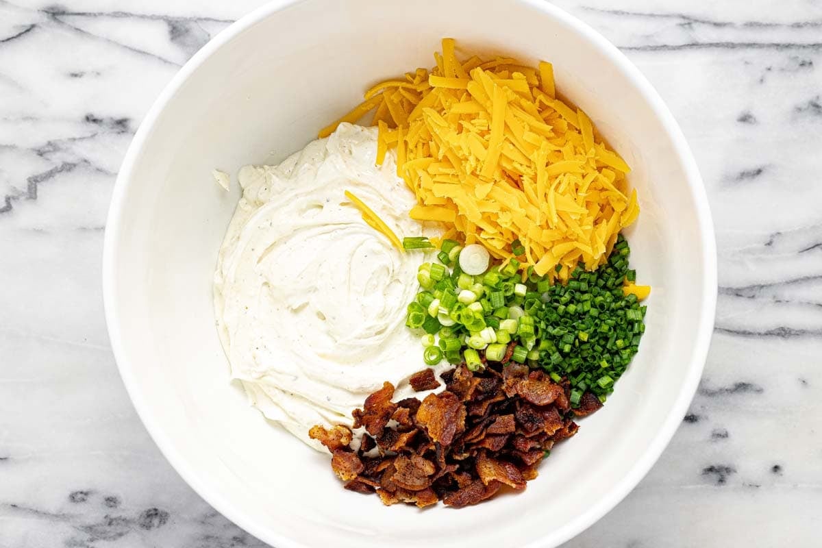 Large bowl filled with cheese, green onion, chives, bacon, and a cream cheese mixture. 