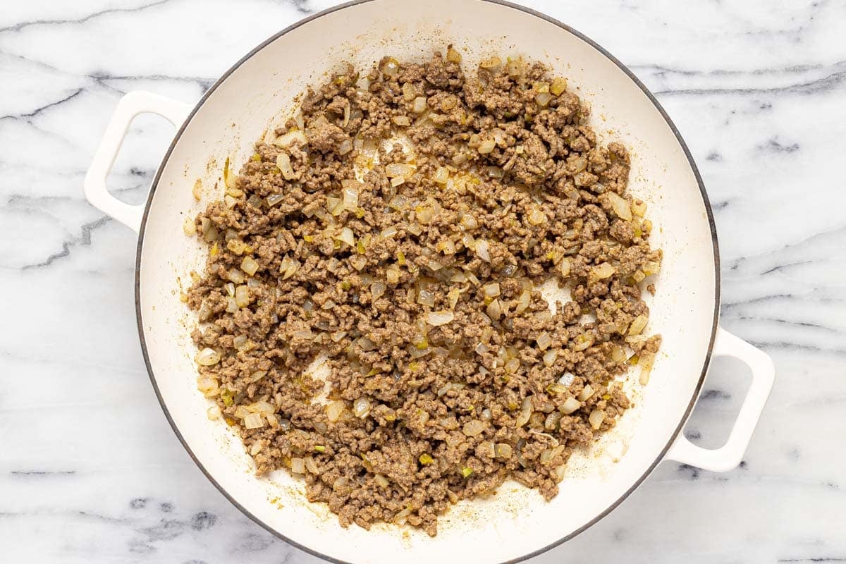 Large saute pan with browned ground beef and diced onion. 