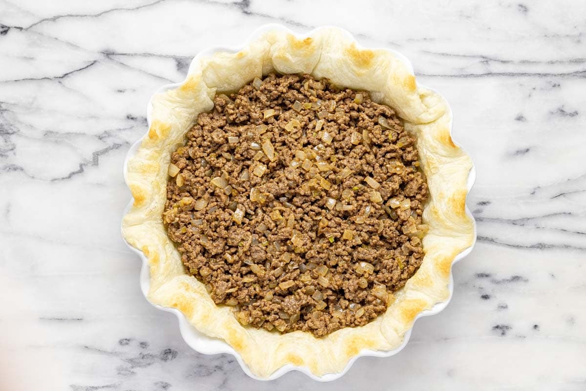 Cooked puff pastry dough in a pie pan with a ground beef mixture in it. 